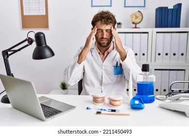 Young Hispanic Dentist Man Working At Medical Clinic With Hand On Head For Pain In Head Because Stress. Suffering Migraine. 