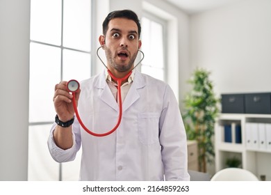 Young hispanic doctor man with beard holding stethoscope auscultating afraid and shocked with surprise and amazed expression, fear and excited face.  - Shutterstock ID 2164859263