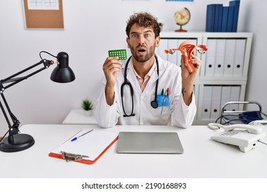 Young Hispanic Doctor Man Holding Female Genital Organ And Birth Control Pills In Shock Face, Looking Skeptical And Sarcastic, Surprised With Open Mouth 