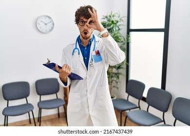 Young Hispanic Doctor Man At Waiting Room Doing Ok Gesture Shocked With Surprised Face, Eye Looking Through Fingers. Unbelieving Expression. 