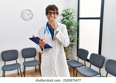 Young Hispanic Doctor Man At Waiting Room Laughing And Embarrassed Giggle Covering Mouth With Hands, Gossip And Scandal Concept 