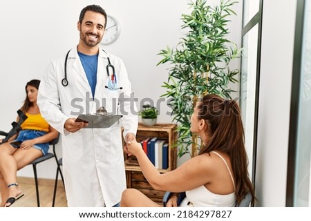 Young hispanic doctor and patient handshake at medical clinic waiting room.