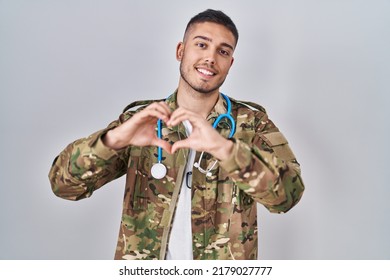 Young hispanic doctor wearing camouflage army uniform smiling in love doing heart symbol shape with hands. romantic concept.  - Powered by Shutterstock