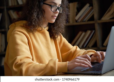 Young hispanic ethnic teen girl college student using laptop computer typing studying working online. Serious millennial woman wear glasses doing internet research elearning at home library office.