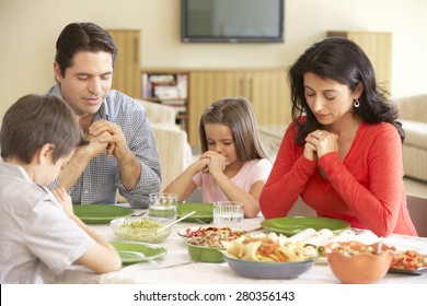 Young Hispanic Family Saying Prayers Before Meal At Home