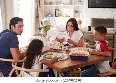 Young Hispanic Family Sitting At Dining Table Eating Dinner Together