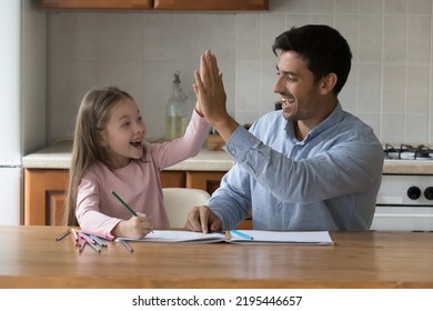 Young Hispanic Father Sit At Table In Kitchen Giving High Five Praising His Cute Preschool Talented Daughter For Success In Paintings. Family Creative Pastime, Children Development, Support Concept