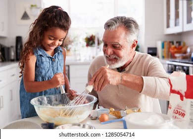 Young Hispanic girl and her grandad whisking cake mixture together at the kitchen table, close up - Powered by Shutterstock