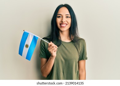 Young hispanic girl holding argentina flag looking positive and happy standing and smiling with a confident smile showing teeth 