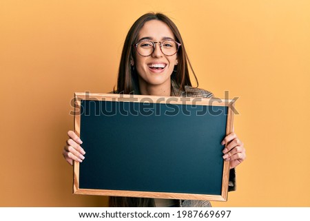 Young hispanic girl holding blackboard smiling and laughing hard out loud because funny crazy joke. 