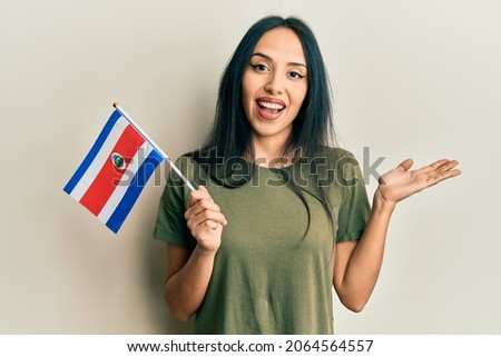 Young hispanic girl holding costa rica flag celebrating achievement with happy smile and winner expression with raised hand 