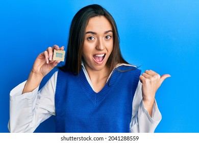 Young Hispanic Girl Holding Cpu Computer Processor Pointing Thumb Up To The Side Smiling Happy With Open Mouth 