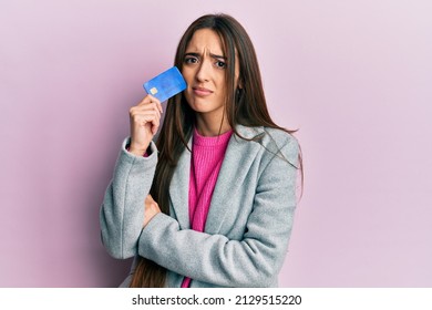 Young Hispanic Girl Holding Credit Card Clueless And Confused Expression. Doubt Concept. 