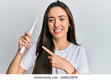 Young hispanic girl holding electric toothbrush smiling happy pointing with hand and finger 