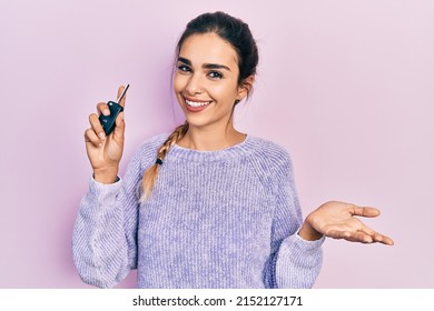 Young hispanic girl holding key of new car celebrating achievement with happy smile and winner expression with raised hand 