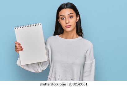 Young Hispanic Girl Holding Notebook Thinking Attitude And Sober Expression Looking Self Confident 