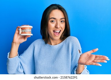 Young Hispanic Girl Holding Orthodontic Celebrating Achievement With Happy Smile And Winner Expression With Raised Hand 