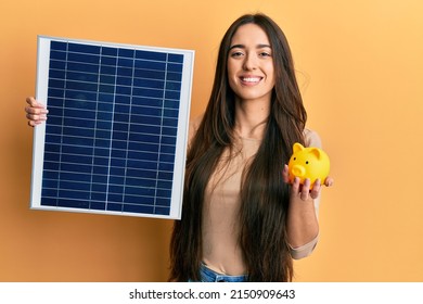 Young hispanic girl holding photovoltaic solar panel and piggy bank smiling with a happy and cool smile on face. showing teeth. 