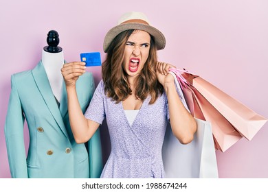 Young Hispanic Girl Holding Shopping Bags And Credit Card Angry And Mad Screaming Frustrated And Furious, Shouting With Anger. Rage And Aggressive Concept. 