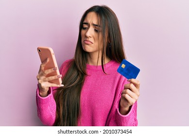 Young Hispanic Girl Holding Smartphone And Credit Card Depressed And Worry For Distress, Crying Angry And Afraid. Sad Expression. 