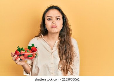 Young Hispanic Girl Holding Strawberries Depressed And Worry For Distress, Crying Angry And Afraid. Sad Expression. 