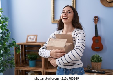 Young Hispanic Girl Opening Cardboard Box Smiling And Laughing Hard Out Loud Because Funny Crazy Joke. 