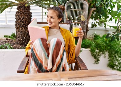 Young Hispanic Girl Reading Book And Drinking Orange Juice At The Terrace.