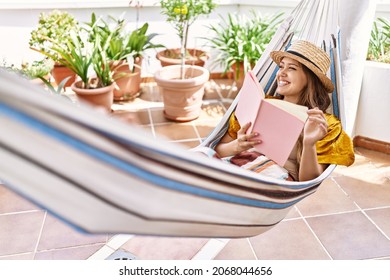 Young Hispanic Girl Reading Book Lying On Hammock At The Terrace.