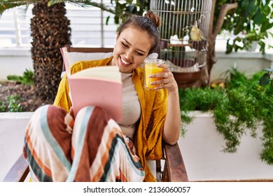 Young Hispanic Girl Reading Book And Drinking Orange Juice At The Terrace.