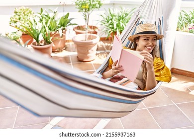 Young Hispanic Girl Reading Book Lying On Hammock At The Terrace.