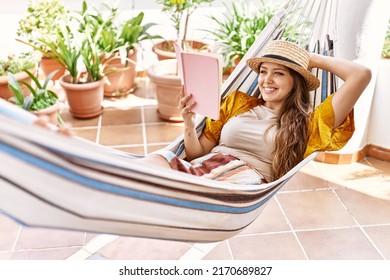 Young Hispanic Girl Reading Book Lying On Hammock At The Terrace.