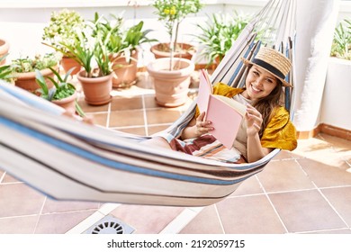 Young Hispanic Girl Reading Book Lying On Hammock At The Terrace.