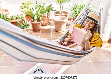 Young Hispanic Girl Reading Book Lying On Hammock At The Terrace.