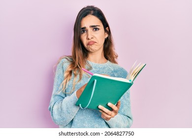 Young hispanic girl reading and writing book depressed and worry for distress, crying angry and afraid. sad expression. 