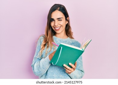 Young Hispanic Girl Reading And Writing Book Winking Looking At The Camera With Sexy Expression, Cheerful And Happy Face. 