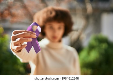 Young hispanic girl with serious expression holding purple awareness ribbon at the city.