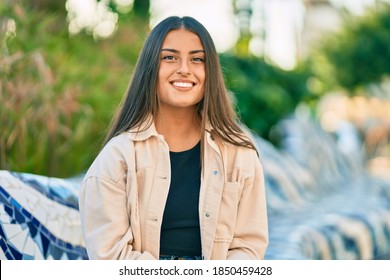 Young hispanic girl smiling happy sitting on the bench at the park.