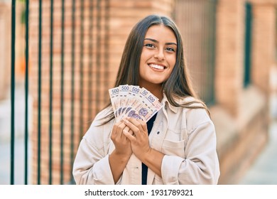 Young hispanic girl smiling happy holding mexican 500 pesos banknotes at the city.