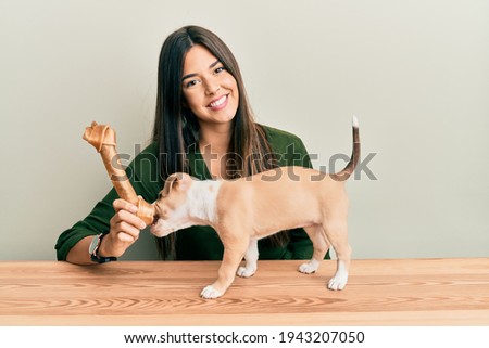 Young hispanic girl smiling happy and playing with dog sitting on the table over isolated white background.