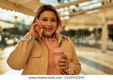 Young hispanic girl talking on the smartphone and drinking coffee at the city.