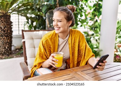 Young hispanic girl using smartphone and drinking orange juice at the terrace. - Powered by Shutterstock