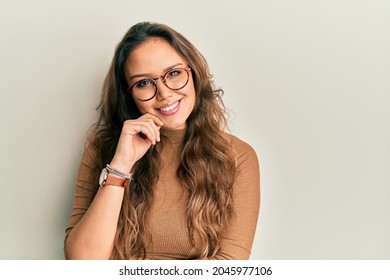 Young Hispanic Girl Wearing Casual Clothes And Glasses Looking Confident At The Camera Smiling With Crossed Arms And Hand Raised On Chin. Thinking Positive. 