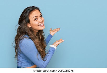 Young hispanic girl wearing casual clothes inviting to enter smiling natural with open hand  - Shutterstock ID 2080186276