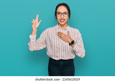 Young hispanic girl wearing casual clothes and glasses smiling swearing with hand on chest and fingers up, making a loyalty promise oath 