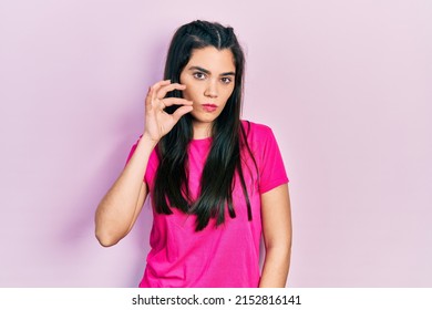 Young hispanic girl wearing casual pink t shirt mouth and lips shut as zip with fingers. secret and silent, taboo talking 