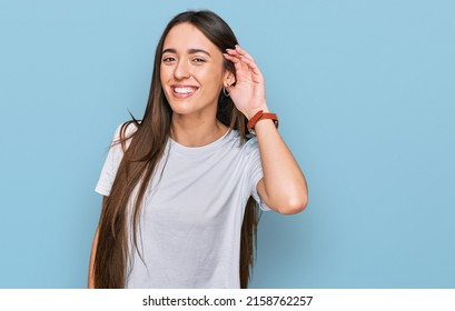 Young Hispanic Girl Wearing Casual White T Shirt Smiling With Hand Over Ear Listening An Hearing To Rumor Or Gossip. Deafness Concept. 