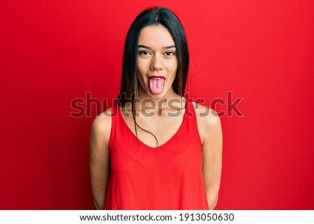 Young hispanic girl wearing casual style with sleeveless shirt sticking tongue out happy with funny expression. emotion concept. 
