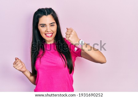 Young hispanic girl wearing casual pink t shirt celebrating surprised and amazed for success with arms raised and eyes closed. winner concept. 
