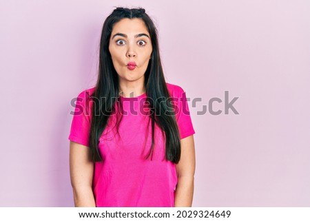 Young hispanic girl wearing casual pink t shirt making fish face with lips, crazy and comical gesture. funny expression. 
