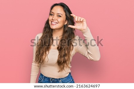Young hispanic girl wearing casual clothes smiling and confident gesturing with hand doing small size sign with fingers looking and the camera. measure concept.  Stock photo © 